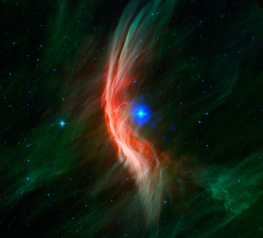 The giant star Zeta Ophiuchi is having a "shocking" effect on the surrounding dust clouds in this infrared image from NASA’s Spitzer Space Telescope. Stellar winds flowing out from this fast-moving star are making ripples in the dust as it approaches, creating a bow shock seen as glowing gossamer threads, which, for this star, are only seen in infrared light.

Zeta Ophiuchi is a young, large and hot star located around 370 light-years away. It dwarfs our own sun in many ways -- it is about six times hotter, eight times wider, 20 times more massive, and about 80,000 times as bright. Even at its great distance, it would be one of the brightest stars in the sky were it not largely obscured by foreground dust clouds.

This massive star is travelling at a snappy pace of about 54,000 mph (24 kilometers per second), fast enough to break the sound barrier in the surrounding interstellar material. Because of this motion, it creates a spectacular bow shock ahead of its direction of travel (to the left). The structure is analogous to the ripples that precede the bow of a ship as it moves through the water, or the sonic boom of an airplane hitting supersonic speeds.

The fine filaments of dust surrounding the star glow primarily at shorter infrared wavelengths, rendered here in green. The area of the shock pops out dramatically at longer infrared wavelengths, creating the red highlights.

A bright bow shock like this would normally be seen in visible light as well, but because it is hidden behind a curtain of dust, only the longer infrared wavelengths of light seen by Spitzer can reach us.

Bow shocks are commonly seen when two different regions of gas and dust slam into one another. Zeta Ophiuchi, like other massive stars, generates a strong wind of hot gas particles flowing out from its surface. This expanding wind collides with the tenuous clouds of interstellar gas and dust about half a light-year away from the star, which is almost 800 times the distance from the sun to